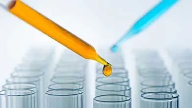 Orange liquid drips from a pipette into a test tube, with a blue-filled pipette in the background.