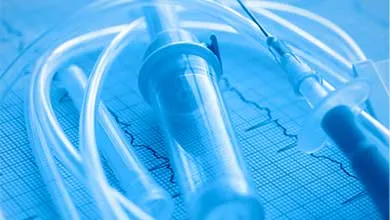 Close-up of an IV drip and syringe on a blue-tinted electrocardiogram readout.