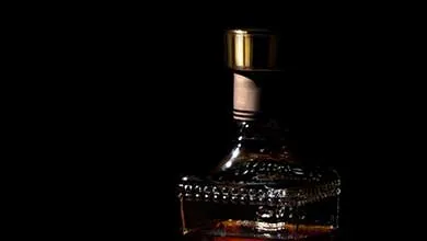 Gold-capped glass liquor bottle centered in dramatic spotlight against a black background.