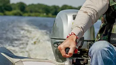 A person steers a small boat with a silver outboard motor, leaving a wake behind.