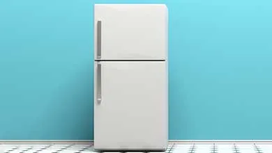 A white two-door refrigerator against a bright blue wall on a black-and-white tiled floor.