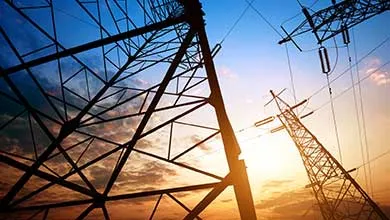 High-voltage electrical transmission towers and power lines silhouetted against a sunset sky.