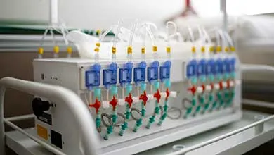 Close-up of a white medical device on a cart, with several clear tubes attached to blue, red, and green ports in rows.
