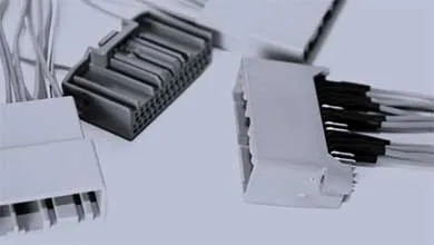 Close-up of several white and dark gray plastic electrical connectors with attached wires on a light-colored surface.