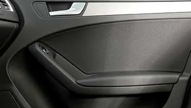 Close-up of a car's dark gray interior door panel with a silver door handle, silver trim, and a grab handle featuring a window switch.