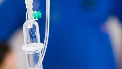 Intravenous drip setup with clear tubing and fluid chamber in a hospital environment.