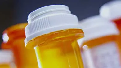 Close-up of an orange prescription bottle with a white child-resistant cap, sharply focused, with blurred prescription bottles in the background.
